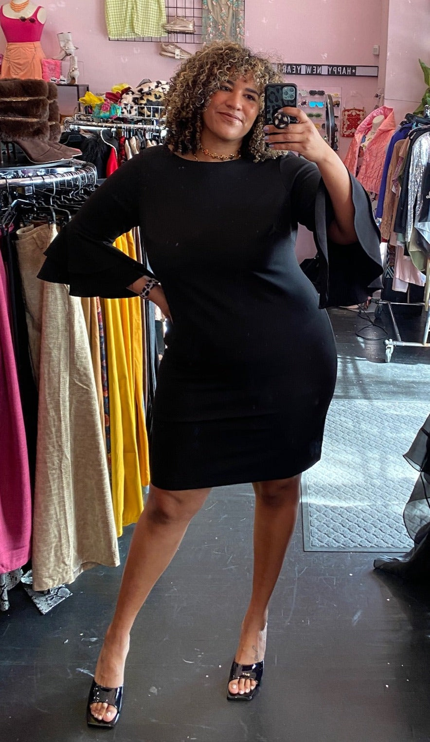 Full-body front view of a size 18W Calvin Klein black ruffle-tiered bell sleeve high neck midi dress styled with black heels on a size 16/18 model.