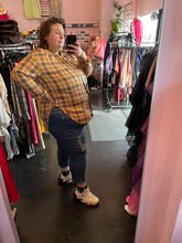 Load image into Gallery viewer, Full-body side view showing off the asymmetrical high-low sides of a size 3X Walk of Shame brand yellow, red, and white snap-button closure blouse with drawstring neckline and asymmetrical side details styled with jeans and sneakers  on a size 24 model.

