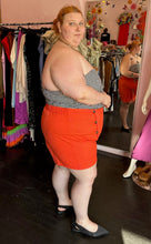 Load image into Gallery viewer, Full-body side view of a pair of size 4X Rebdolls vibrant orange shorts with tortoiseshell button details and pockets styled with a strapless gingham blouse and black pointed flats on a size 22/24 model.
