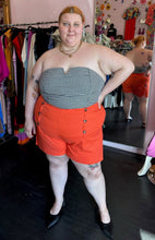 Load image into Gallery viewer, Full-body front view of a pair of size 4X Rebdolls vibrant orange shorts with tortoiseshell button details and pockets styled with a strapless gingham blouse and black pointed flats on a size 22/24 model.
