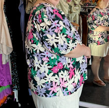 Load image into Gallery viewer, Side view showing off the puff sleeves and small side slit of a size 28 Eloquii black, white, purple, pink, and green geometric floral subtle puff sleeve blouse styled with white shorts on a size 22/24 model.

