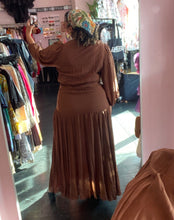 Load image into Gallery viewer, Full-body back view of a size 1 Fashion to Figure brown tiered maxi wrap dress with a tortoiseshell belt buckle styled with black heels on a size 16/18 model.
