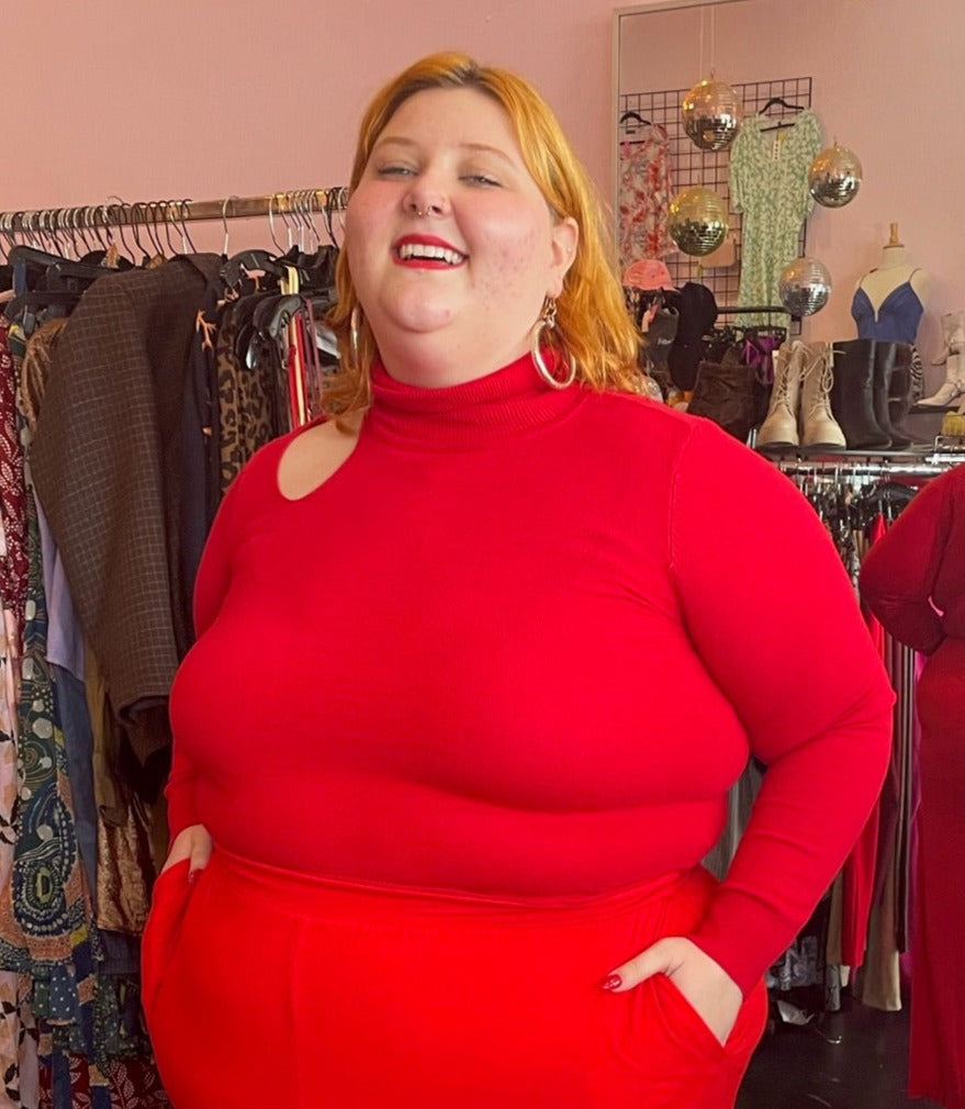 Front view of a size L Catherine Malandrino vibrant red turtleneck sweater with a shoulder cut out styled with red pants on a size 22/24 model.