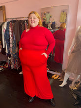 Load image into Gallery viewer, Full-body front view of a size L Catherine Malandrino vibrant red turtleneck sweater with a shoulder cut out styled with red pants on a size 22/24 model.
