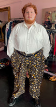 Load image into Gallery viewer, Full-body front view of a pair of size 6XL Big Bud Press dark brown, mustard yellow, and white mixed mushroom and floral pattern work pants styled with a cream button-up shirt and black loafers on a size 24/26 model.
