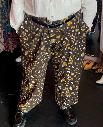 Front view of a pair of size 6XL Big Bud Press dark brown, mustard yellow, and white mixed mushroom and floral pattern work pants styled with a cream button-up shirt and black loafers on a size 24/26 model.