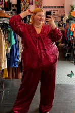 Load image into Gallery viewer, Additional full-body front view of a size 28 Eloquii hot pink sequin jumpsuit with tie-front bust detail, pockets, and a full lining styled with black boots on a size 22/24 model.
