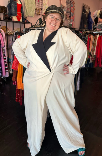 Full-body front view of a size 28 Eloquii cream and black tuxedo-style jumpsuit with draped wide leg styled with a black, white, and gold newsboy cap on a size 24 model.