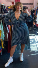 Load image into Gallery viewer, Full-body front view of a size 3X Black Ivy brand dark teal and white vertical striped faux wrap midi dress with high-low hemline styled with white sneakers on a size 16/18 model.
