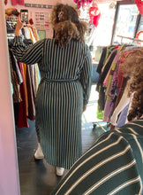 Load image into Gallery viewer, Full-body back view of a size 3X Black Ivy brand dark teal and white vertical striped faux wrap midi dress with high-low hemline styled with white sneakers on a size 16/18 model.
