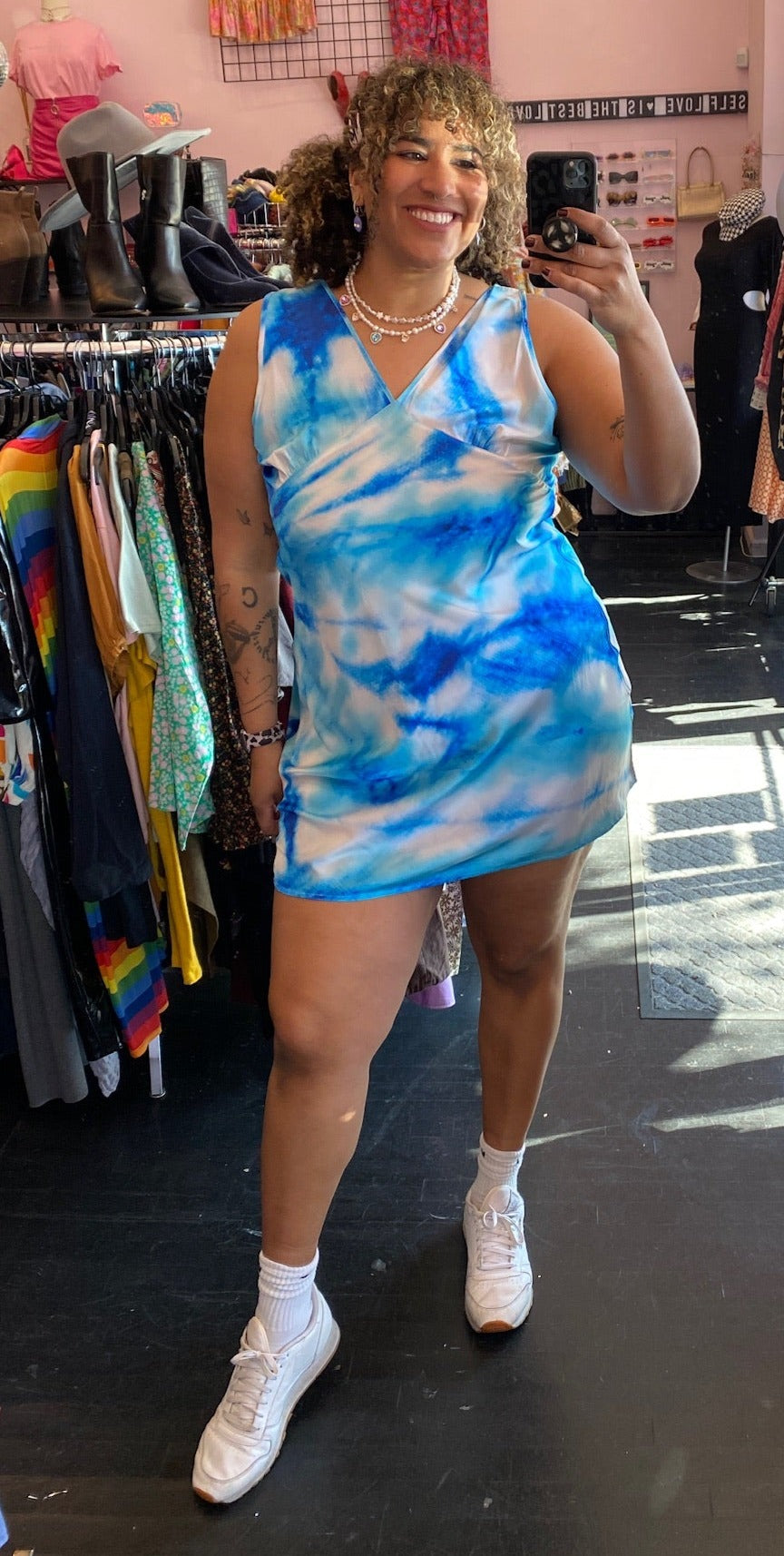 Full-body front view of a size 18 Collusion brand bright blue, light blue, and white acid wash tie dye mini dress styled with white sneakers on a size 16/18 model.