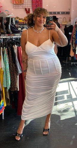 Full-body front view of a size 3X Finesse brand white ruched maxi dress with corset-style waist boning styled with black heels on a size 16/18 model.