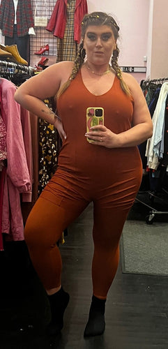 Full-body front view of a size 3X Nike copper colored one-piece active jumpsuit with built in bar and shorts detail on a size 14/16 model.