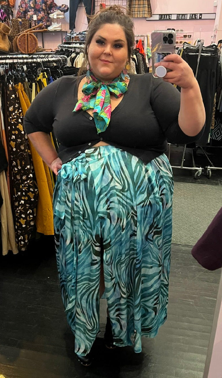 Full-body front view of a size 22 Novella brand blue and teal zebra print wrap maxi skirt styled with a black button up cardigan on a size 22/24 model.