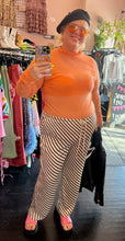 Load image into Gallery viewer, Additional full-body front view of a pair of size XXL H&amp;M off-white and black diagonally striped silky drawstring pants styled with an orange sheer mesh mockneck top, a black beret, and pink slides on a size 16/18 model.
