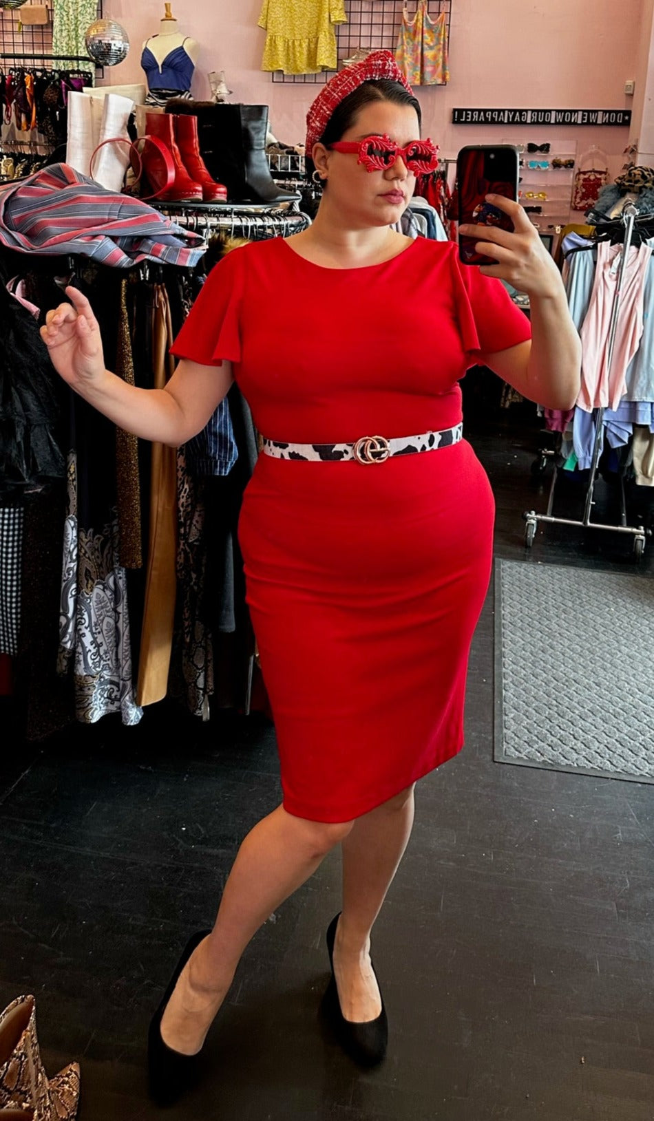 Full-body front view of a size 14 Calvin Klein red flutter sleeve sheath midi dress styled with black pumps, a cow-print belt, and red accessories on a size 14/16 model.