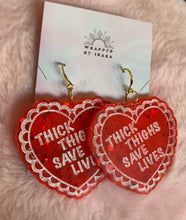 Load image into Gallery viewer, Sidelong close up on the red transluscent valentine heart earrings that read &quot;Thick Thighs Save Lives&quot; with chunky glitter inside!
