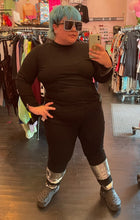 Load image into Gallery viewer, Additional full-body front view of a pair of size 16 Eloquii black denim straight leg jeans with silver sequin details at the ankles styled with a black turtleneck and black crocs on a size 16/18 model.
