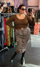 Load image into Gallery viewer, Additional full-body front view of a size XL (fits up to size 24) GANNI deep gold metallic ribbed knit sweater styled with zip-up leopard skirt and brown belt on a size 14/16 model. The photo is taken inside in overhead lighting.
