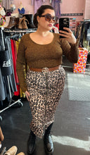 Load image into Gallery viewer, Full-body front view of a size XL (fits up to size 24) GANNI deep gold metallic ribbed knit sweater styled with zip-up leopard skirt and brown belt on a size 14/16 model. The photo is taken inside in overhead lighting.
