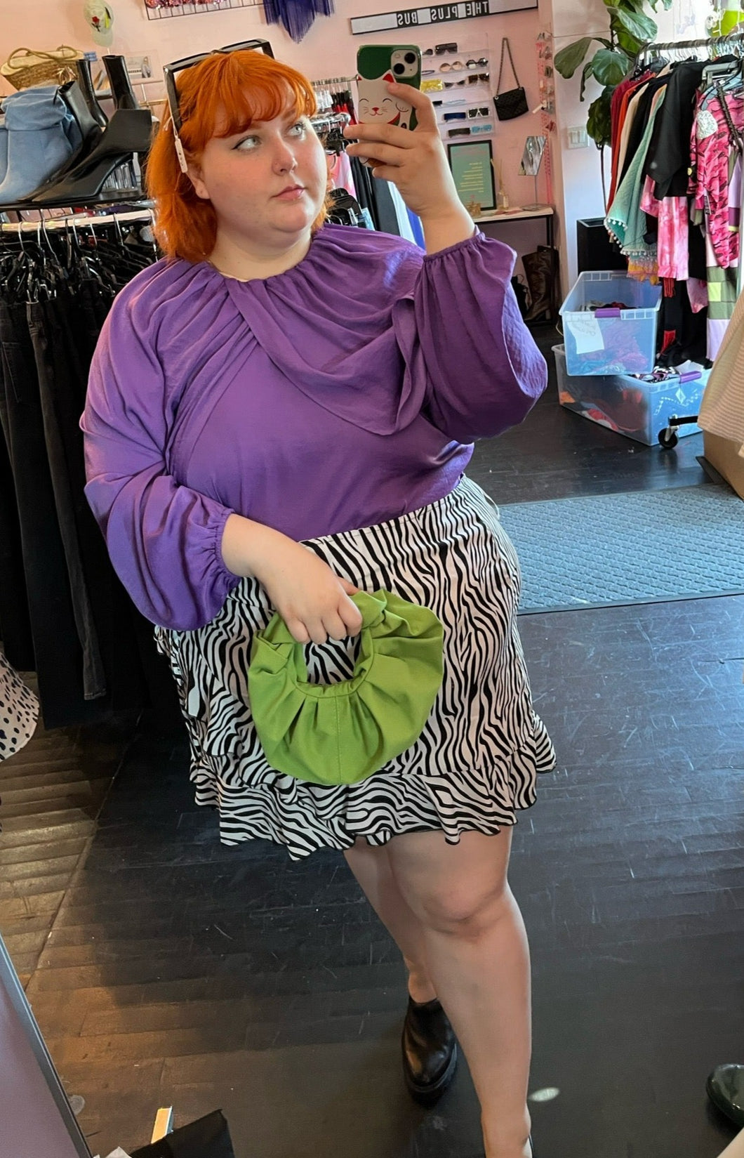 Full-body front view of a size 28 Eloquii vibrant purple draped and gathered blouse with balloon sleeves styled with a zebra ruffled skirt and a green handband on a size 22/24 model.