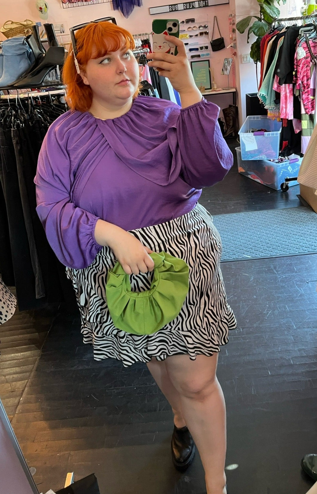 Full-body front view of a size 28 Eloquii vibrant purple draped and gathered blouse with balloon sleeves styled with a zebra ruffled skirt and a green handband on a size 22/24 model.