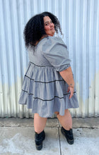 Load image into Gallery viewer, Full-body back view of a size 28 Simply Be brand black and white gingham plaid mini-print tiered prairie dress with black trim and puff sleeves styled with black combat boots on a size 24/26 model. The photo is taken outside in natural lighting.
