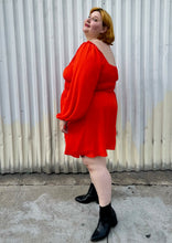 Load image into Gallery viewer, Full-body side view of a size 2X WRAY red-orange scoop neck mini dress with smocked waist and puff sleeve with elastic cuff styled with black boots on a size 22/24 model.
