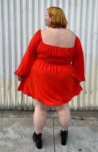 Load image into Gallery viewer, Full-body back view of a size 2X WRAY red-orange scoop neck mini dress with smocked waist and puff sleeve with elastic cuff styled with black boots on a size 22/24 model.
