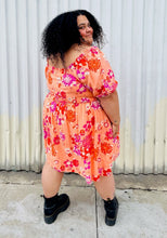 Load image into Gallery viewer, Full-body back view of a size 4X BP peach, pink, and orange floral off-shoulder mini dress with subtle high-low hemline styled with black combat boots on a size 24/26 model.
