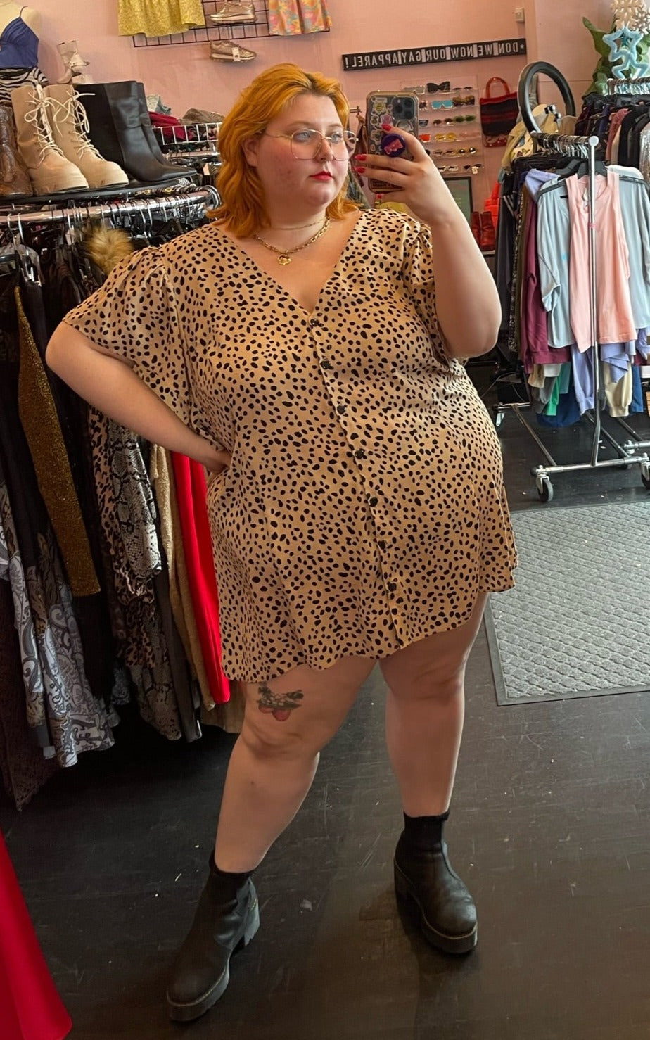 Full-body front view of a size 22/24 light brown and black leopard pattern button-up mini dress styled with black boots on a size 22/24 model.
