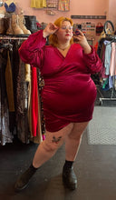 Load image into Gallery viewer, Full-body front view of a size 22 Bloomchic deep red velvet mini dress with draped details and long, puff sleeves styled with black boots on a size 22/24 model. This photo is taken inside with overhead lighting.
