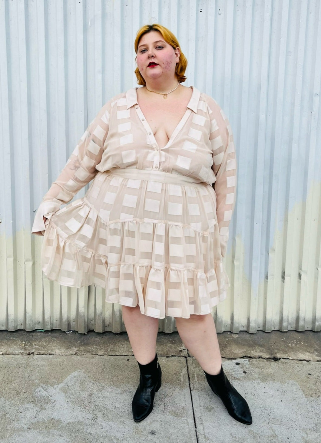 Full-body front view of a size 26 ASOS cream colored square pattern sheer mesh tiered button-up shirt dress with cream lining styled with black boots on a size 22/24 model. The photo is taken outside in natural lighting.
