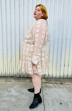 Load image into Gallery viewer, Full-body side view of a size 26 ASOS cream colored square pattern sheer mesh tiered button-up shirt dress with cream lining styled with black boots on a size 22/24 model. The photo is taken outside in natural lighting.
