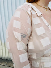 Load image into Gallery viewer, Close up view of the square pattern mesh overlay of a size 26 ASOS cream colored square pattern sheer mesh tiered button-up shirt dress with cream lining on a size 22/24 model. The photo is taken outside in natural lighting.
