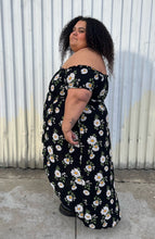 Load image into Gallery viewer, Full-body side view of a size 2X Forever 21 black, white, and yellow daisy pattern smocked bust off-shoulder maxi dress with high-low tulip hem styled with black combat boots on a size 24/26 model. The photo is taken outside in natural lighting.
