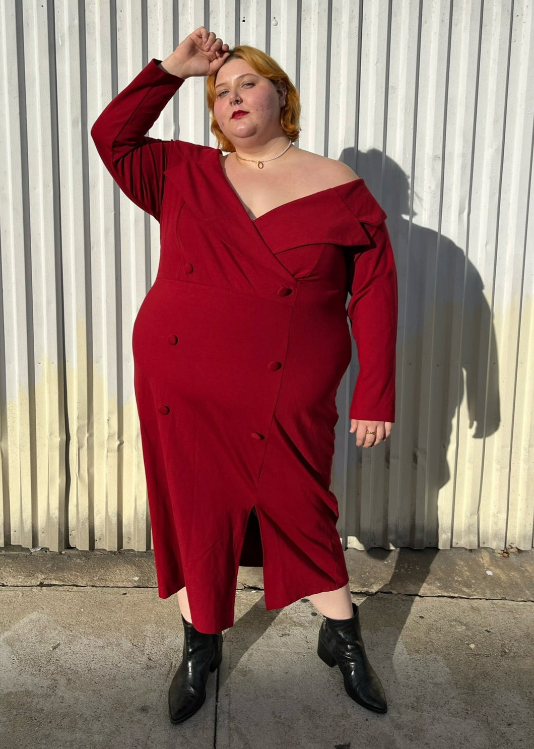 Full-body front view of a size 28 Eloquii deep red off-shoulder blazer style midi dress with collar and subtle front slit styled with black boots on a size 22/24 model.
