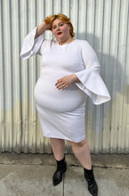 Load image into Gallery viewer, Additional full-body front view showing off the length and flow of the bell sleeves of a size 24 Eloquii white shift dress with long bell sleeves styled with black pointy boots on a size 22/24 model. The photo is taken outside in natural lighting.
