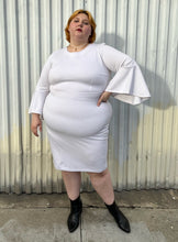 Load image into Gallery viewer, Full-body front view of a size 24 Eloquii white shift dress with long bell sleeves styled with black pointy boots on a size 22/24 model. The photo is taken outside in natural lighting.
