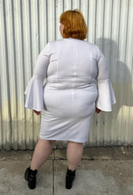 Load image into Gallery viewer, Full-body back view of a size 24 Eloquii white shift dress with long bell sleeves styled with black pointy boots on a size 22/24 model. The photo is taken outside in natural lighting.
