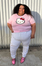 Load image into Gallery viewer, Full-body front view of a size 5XL SHEIN x Hello Kitty baby pink tee with Hello Kitty graphic and black piping at the neckline styled with white denim and pink loafers on a size 24/26 model.
