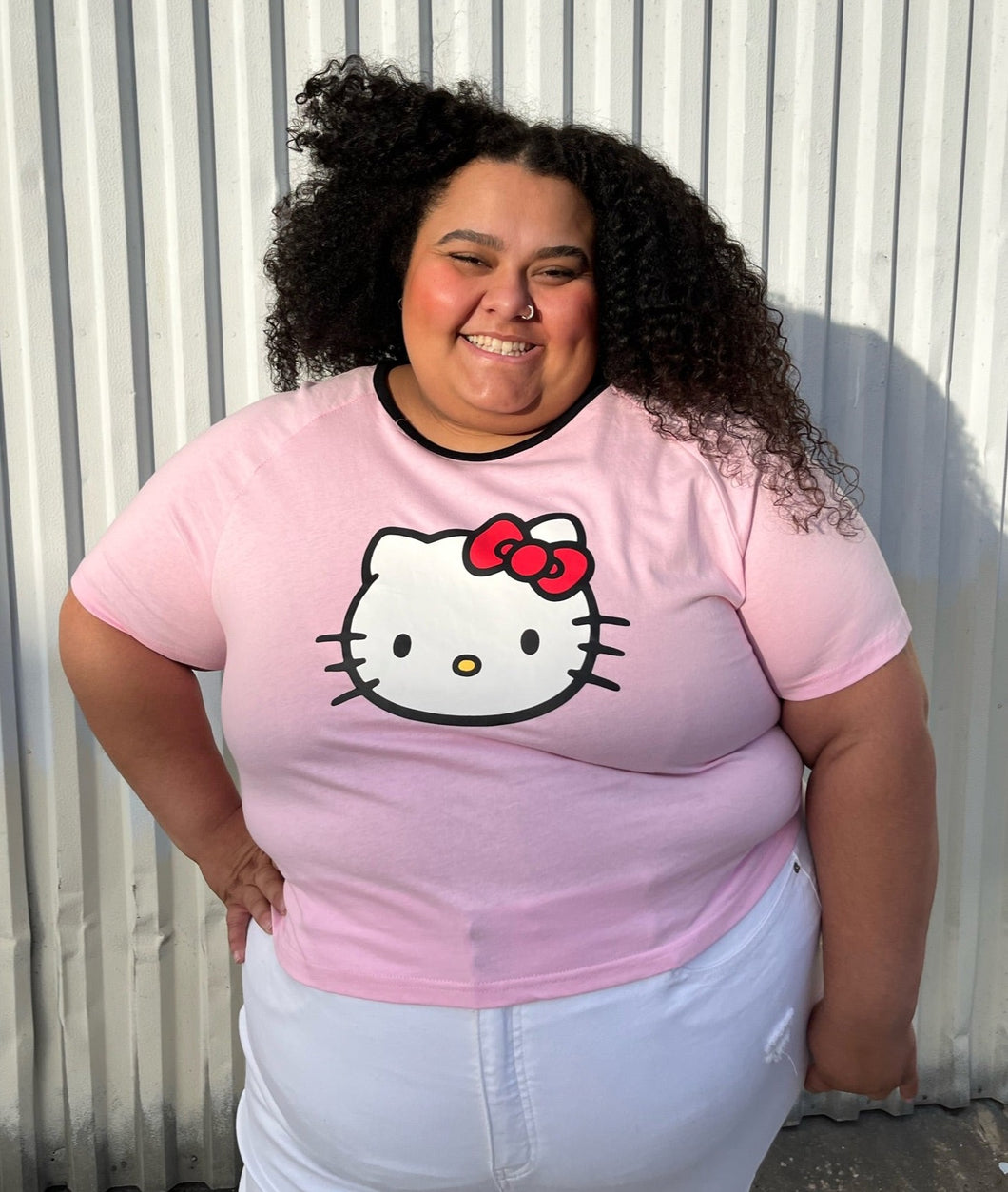 Front view of a size 5XL SHEIN x Hello Kitty baby pink tee with Hello Kitty graphic and black piping at the neckline styled with white denim on a size 24/26 model.