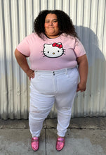 Load image into Gallery viewer, Full-body front view of a pair of size 24 Fashion to Figure slight high-waisted white distressed denim with the distressing focused at the knee and shins styled with a pink tee and pink loafers on a size 24/26 model.
