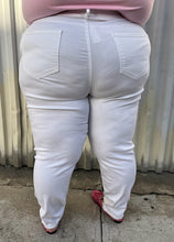 Load image into Gallery viewer, Back view of a pair of size 24 Fashion to Figure slight high-waisted white distressed denim with the distressing focused at the knee and shins styled with a pink tee and pink loafers on a size 24/26 model.
