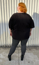 Load image into Gallery viewer, Full-body back view of a size 24 ASOS black plisse pleated tee styled over black and white windowpane pattern pants with black point boots on a size 22/24 model. The photo is taken outside in natural lighting.
