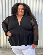 Load image into Gallery viewer, Front view of a size 24 ASOS black v-neck baby doll top with sheer long sleeves styled with white denim on a size 24/26 model. The photo is taken outside in natural lighting.
