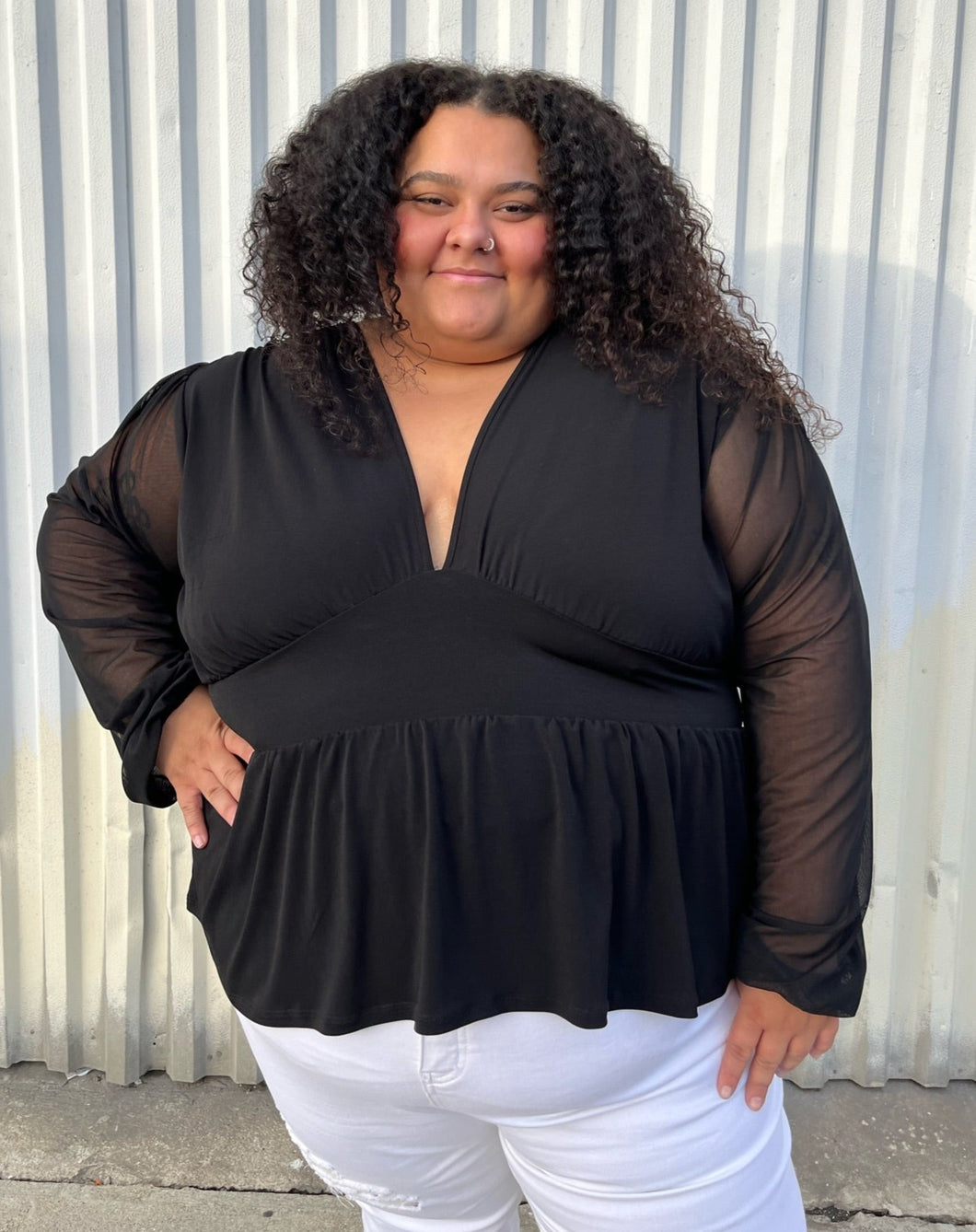 Front view of a size 24 ASOS black v-neck baby doll top with sheer long sleeves styled with white denim on a size 24/26 model. The photo is taken outside in natural lighting.