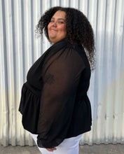 Load image into Gallery viewer, Side view showing off the sleeve of a size 24 ASOS black v-neck baby doll top with sheer long sleeves styled with white denim on a size 24/26 model. The photo is taken outside in natural lighting.
