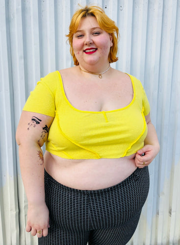 Front view of a size XXL Urban Outfitters size XXL (fits up to 20/22) lemon yellow exposed seam detail crop top with cap sleeves styled with black and white windowpane plaid pants on a size 22/24 model. The photo is taken outside in natural lighting.
