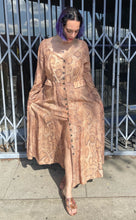 Load image into Gallery viewer, Addtional full-body front view showing off the slit and width of a size 12 Mara Hoffman tan, brown, and white snake print button-up maxi dress with hip pocket details styled with snake print heels on a size 10 model. The photo is taken outside in natural lighting.
